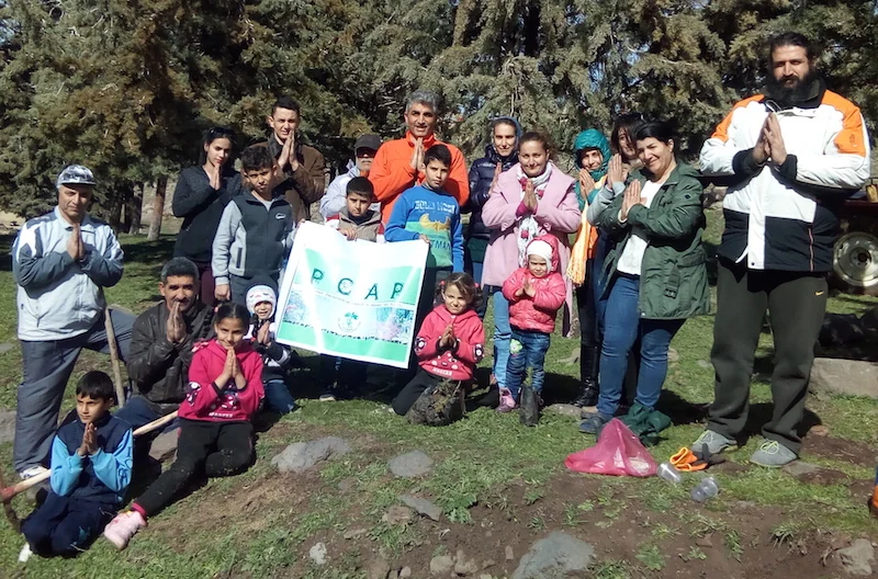 Families and volunteers with a PCAP banner beside a planted sapling in Syria